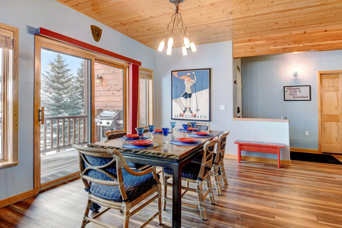A cozy dining area with a family-sized table, artwork on the wall, and large windows letting in natural light and snowy views—perfect for casual gatherings, meals, or board game nights.