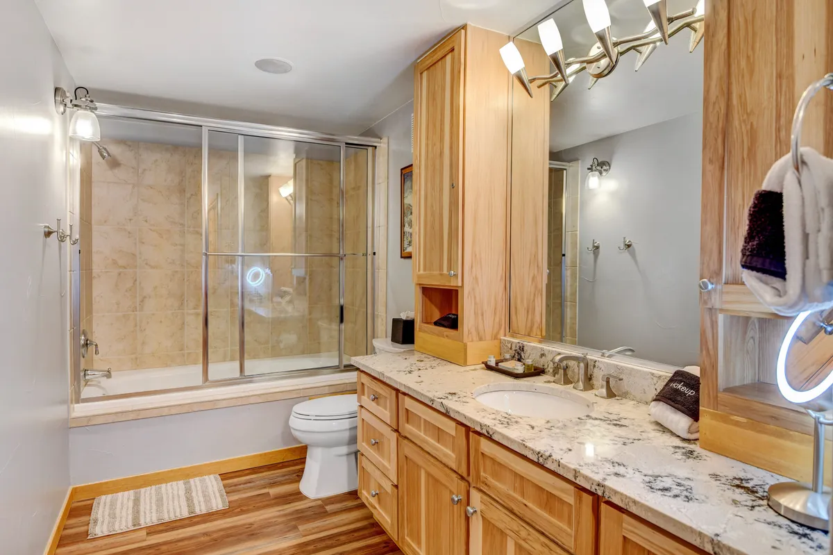 A modern bathroom with a granite-topped vanity, glass shower enclosure, and wooden cabinetry. The space feels fresh, clean, and updated, ideal for both privacy and post-adventure relaxation.