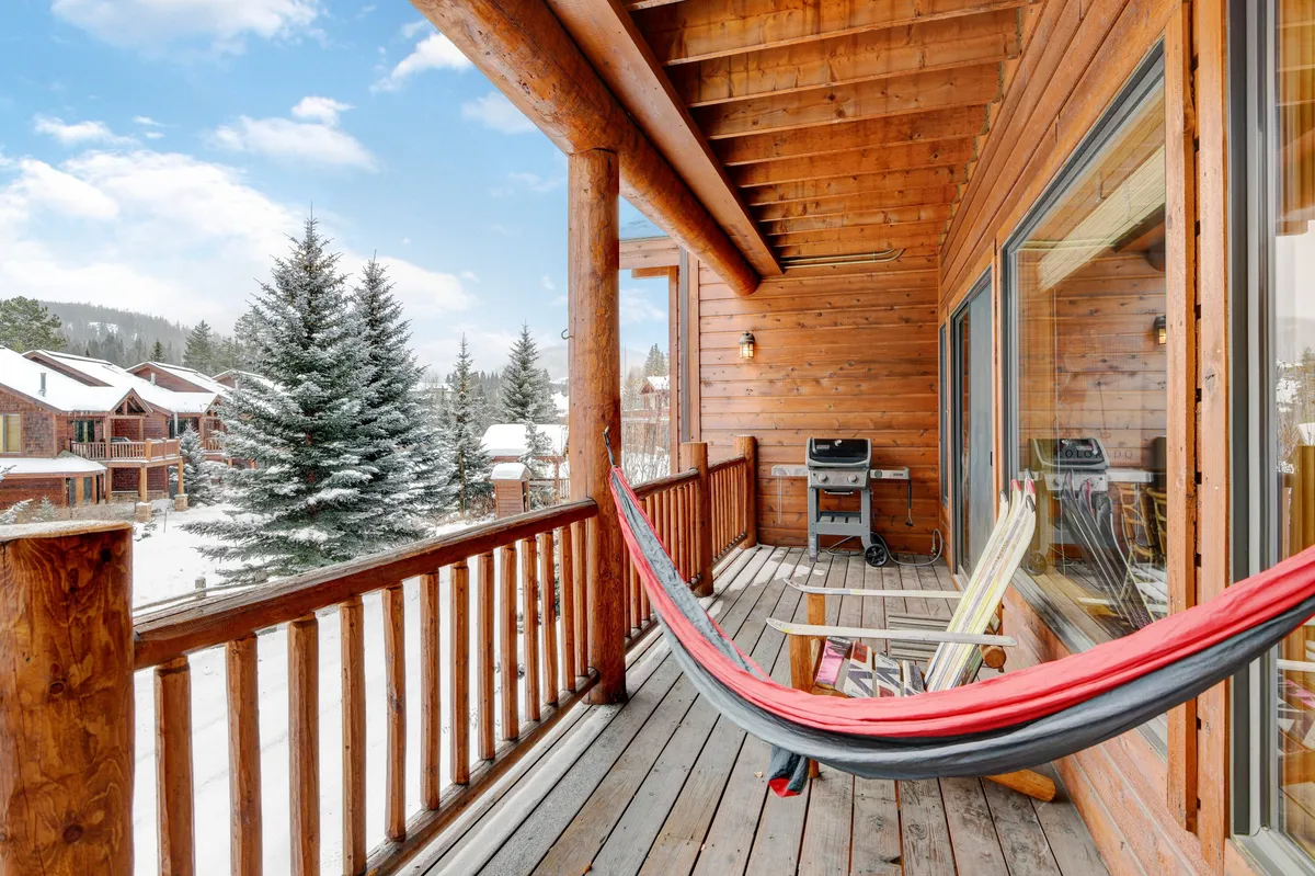 An inviting exterior shot of a patio or deck featuring a hammock, wooden railings, a barbecue grill, and breathtaking mountain vistas. The scene suggests a tranquil place to relax, entertain, or take in the scenery, with natural light highlighting the outdoor amenities.
