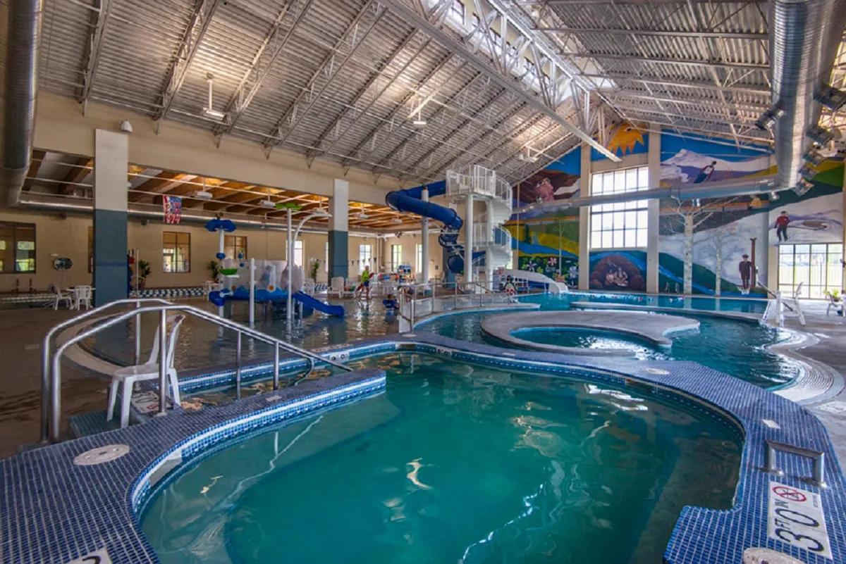 A vibrant indoor recreation center featuring colorful water slides, swimming pools, and children playing. The joyful atmosphere highlights family activities and year-round fun, aligning with the mention of the Grand Park Rec Center's pool and water features.
