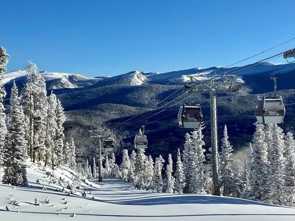 A panoramic mountain view featuring ski lifts gliding over snow-covered slopes, pine trees, and distant peaks bathed in natural light. The scene evokes the grandeur and majesty of the mountain environment surrounding the chalet.
