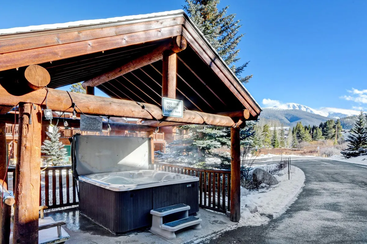 An inviting outdoor hot tub set against a backdrop of mountains and a wooden structure, evoking a sense of tranquility and relaxation. The scene captures guests soaking in the hot tub while admiring the surrounding nature, embodying the idea of resort-style amenities just steps from the home.