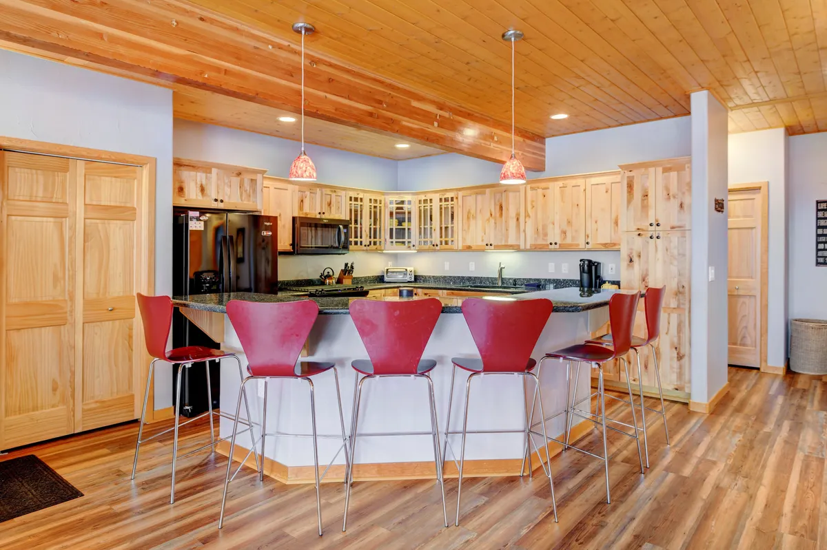 The scene features a modern kitchen island with vibrant red bar stools and stylish pendant lights. The setup emphasizes premium appliances and ample prep space, with a layout ideal for both cooking and casual gatherings. The festive touches hint at the kitchen being a centerpiece for holiday brunches and social occasions.