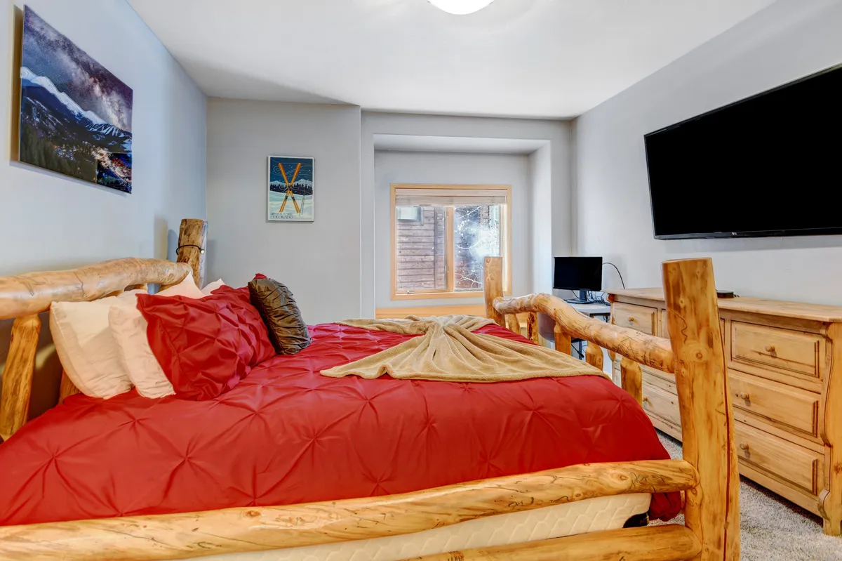 A spacious bedroom featuring a large bed with a rustic log frame, soft bedding, a window allowing natural light to pour in, and a television mounted on the wall. The space exudes comfort and tranquility, ideal for guests seeking restful nights after adventurous days.